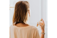 Image A woman from behind spraying perfume on herself.
